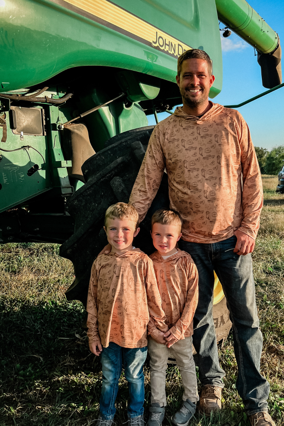 father and 2 sons standing in front of a combine