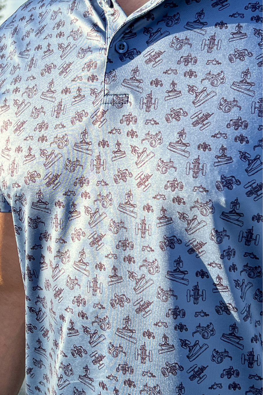 Close up picture of a man wearing a blue polo with a vintage tractor design.