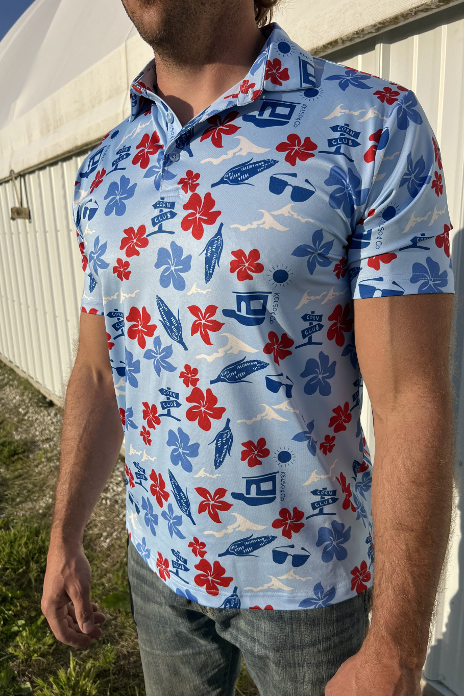 Man standing in front of a building wearing a light blue polo with a red, white and blue Hawaiian inspired print.