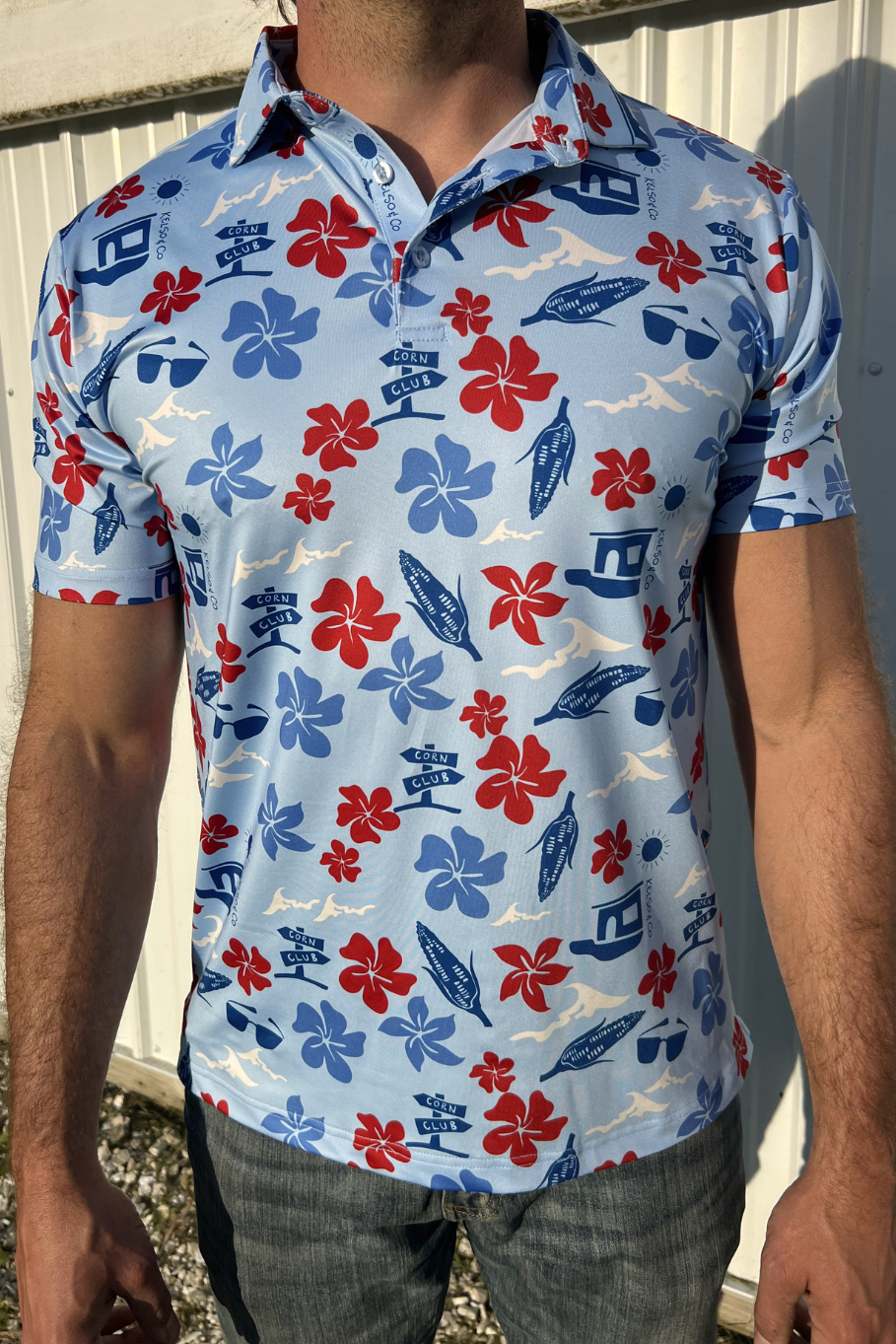 Man standing in front of a building wearing a light blue polo with a red, white and blue Hawaiian inspired print.