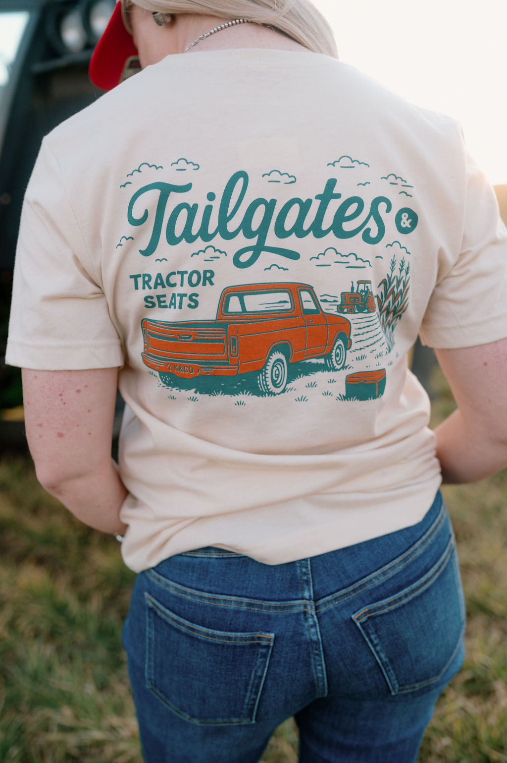 girl wearing a graphic tshirt that says tailgates and tractor seats with an orange vintage truck