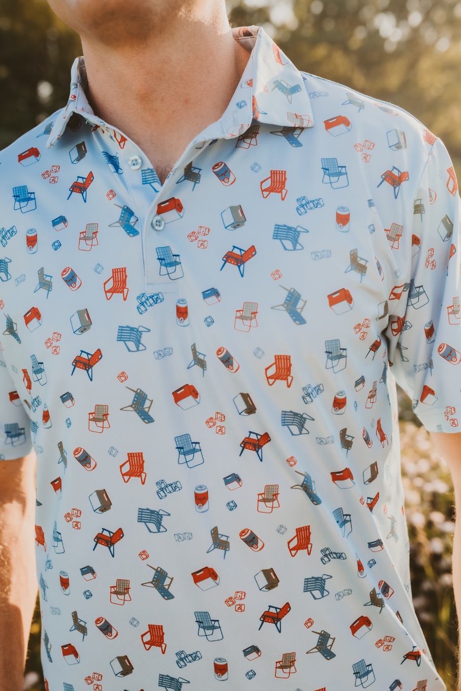 close up pattern of vintage lawn chairs, coolers, ice and a lager on a men's performance polo in light blue