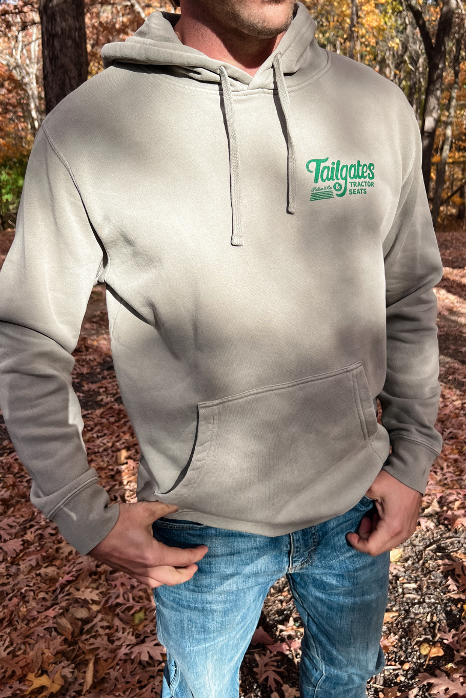guy wearing cement pigmented hoodie with tailgates and tractor seats on left front chest in green