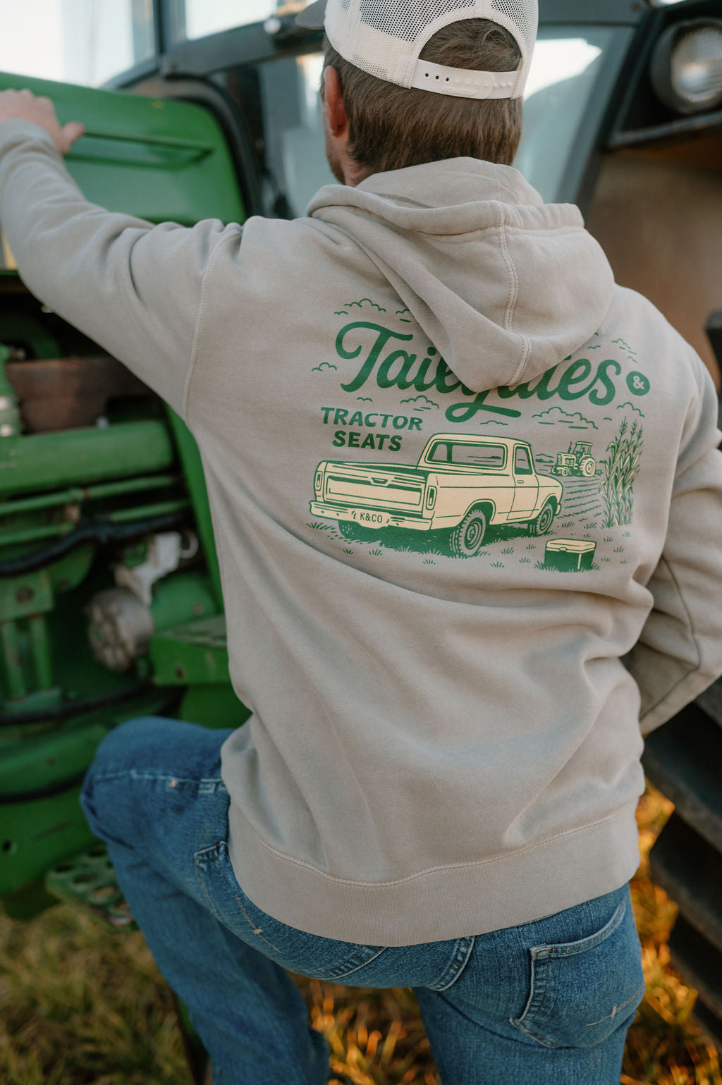 guy stepping up into a tractor with a hoodie on that says tailgates and tractor seats with a vintage pick up truck
