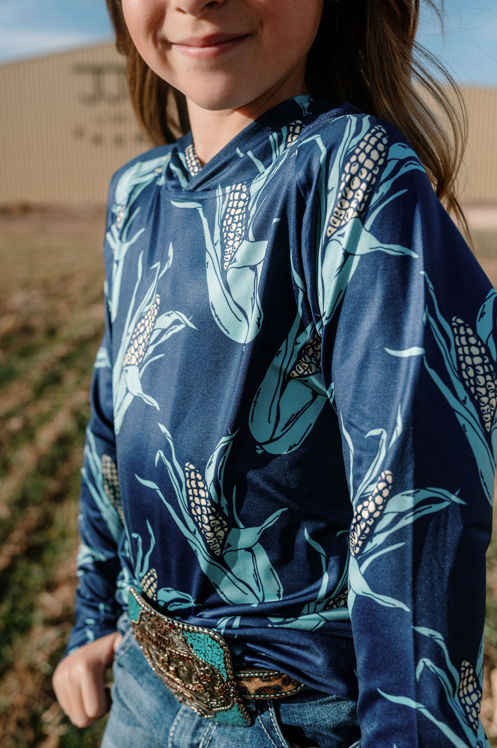 girl wearing our navy kids performance hoodie with large ears of corn all over.