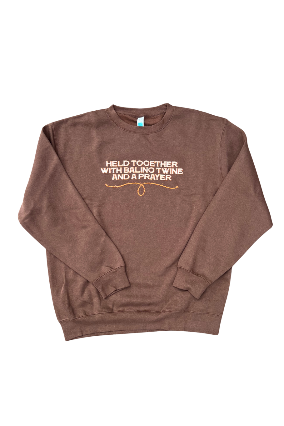 A brown crewneck sweatshirt with a printed graphic on the chest reading 'HELD TOGETHER WITH BAILING TWINE AND A PRAYER' in white and orange, displayed flat against a white background.