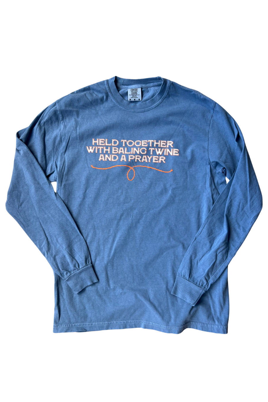 A long-sleeve t-shirt in a medium blue color, featuring the text 'HELD TOGETHER WITH BAILING TWINE AND A PRAYER' in white across the chest.