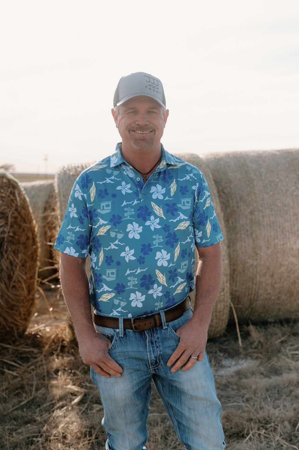 Picture of man standing by hay bales wearing blue Hawaiian inspired polo. 
