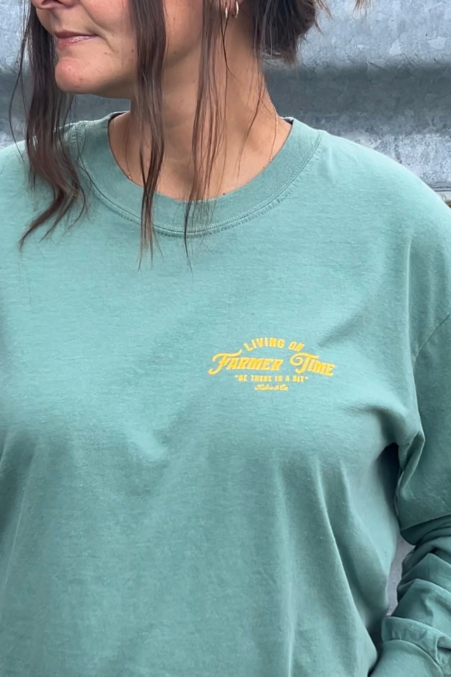 A close-up of a person wearing a light green long-sleeve t-shirt with a yellow embroidered graphic on the left chest that reads 'Living a Fullness Life'.