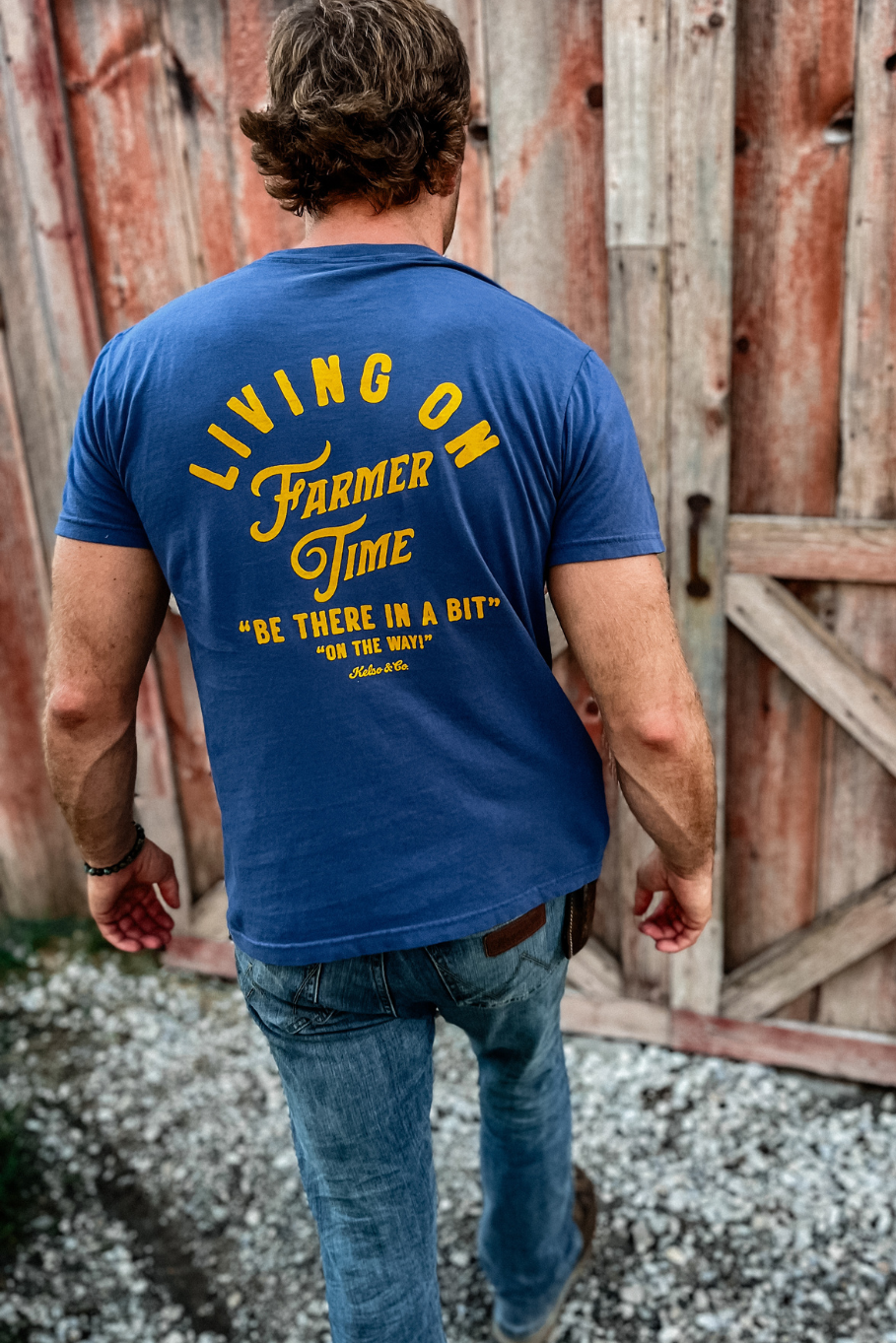 guy standing in front of a barn wearing a graphic tshirt that says &quot;Living on Farmer Time&quot;