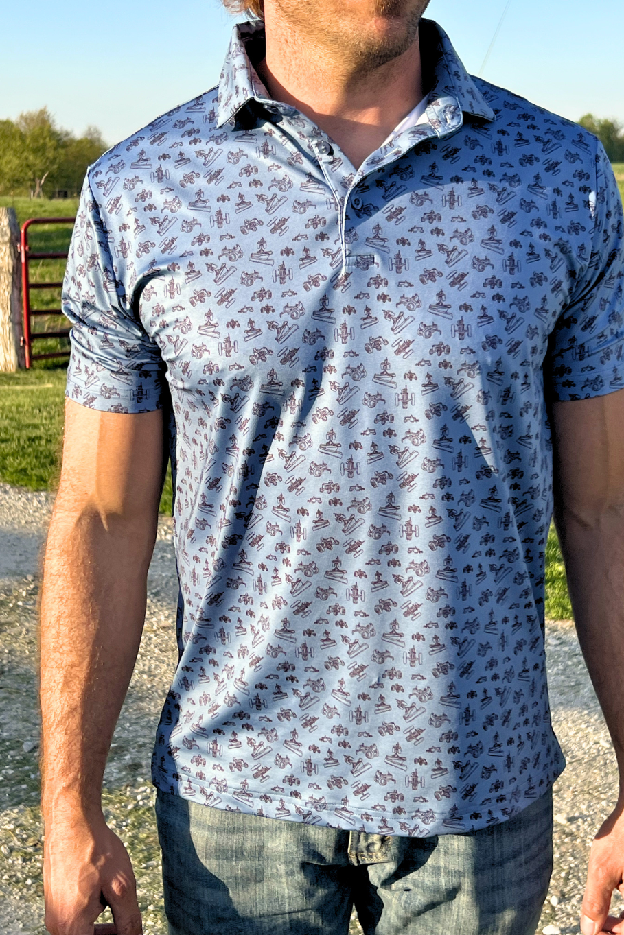 Picture of a man standing wearing a blue polo with a vintage tractor design in front of a fence. 