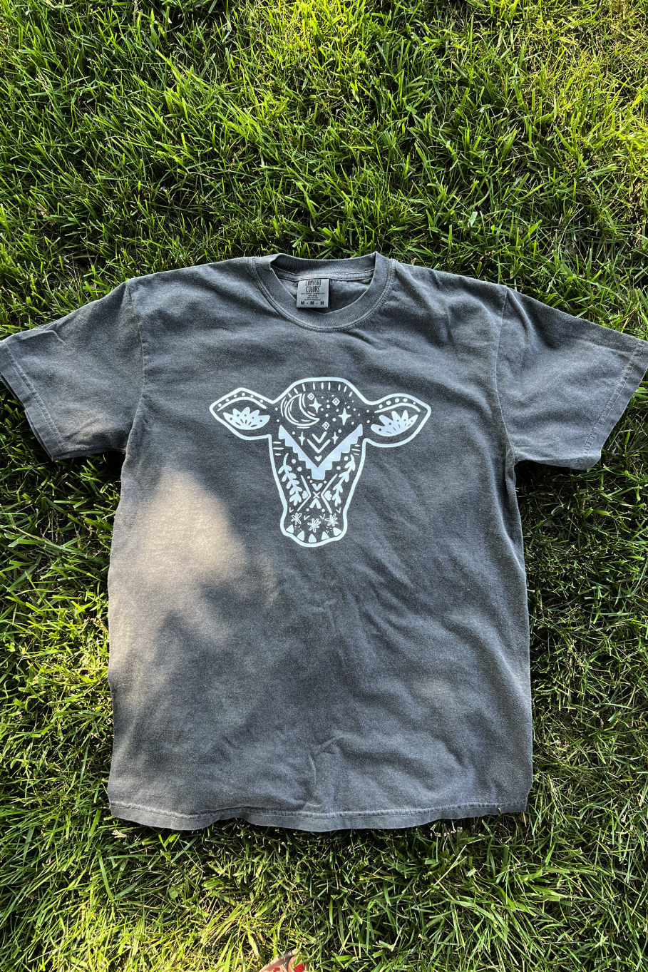 Front of a gray tee with a white, cow head, hand doodled detailed graphic.