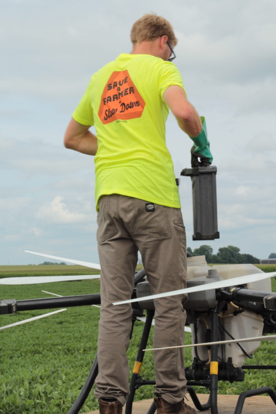 Man wearing save a farmer and slow down neon yellow tshirt while filling up a spraying drone