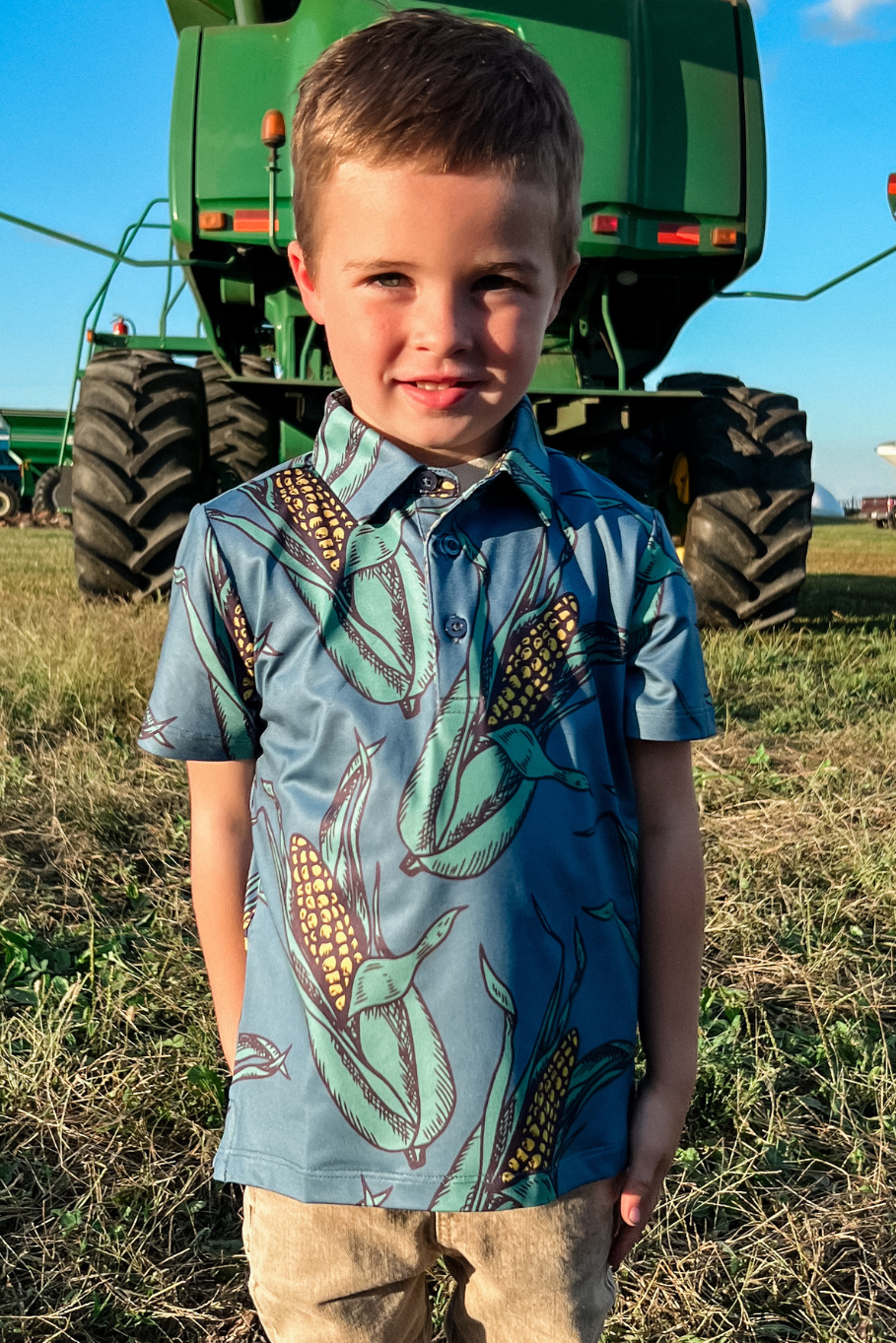 little boy with a corn polo standing behind a john deere combine