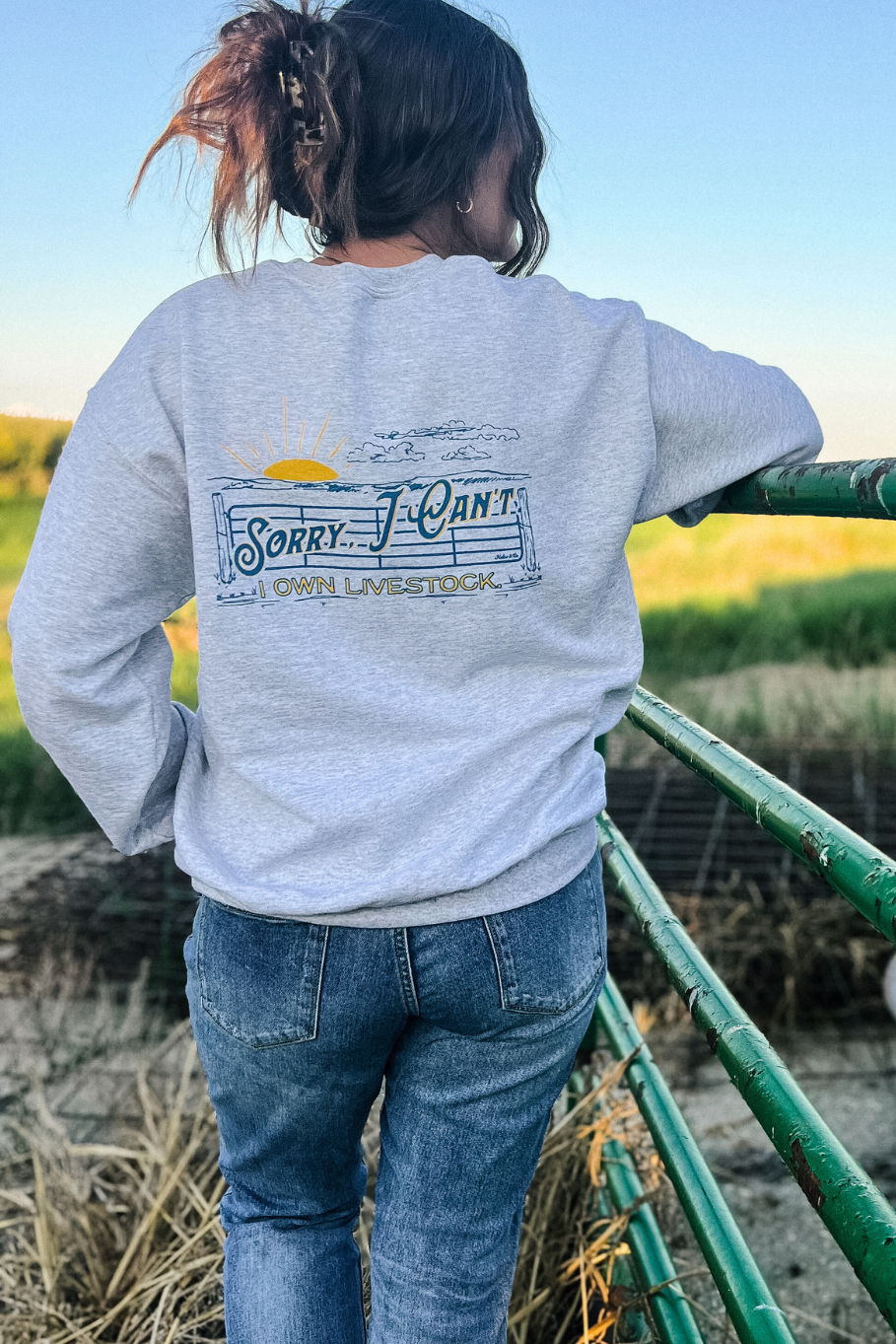 Back of ash gray crewneck with a graphic that has a livestock gate and a sunset that says sorry I can't I own livestock