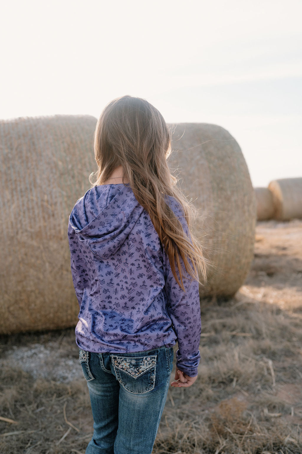 girl on a farm wearing a purple performance hoodie with dark purple antique tractor pattern
