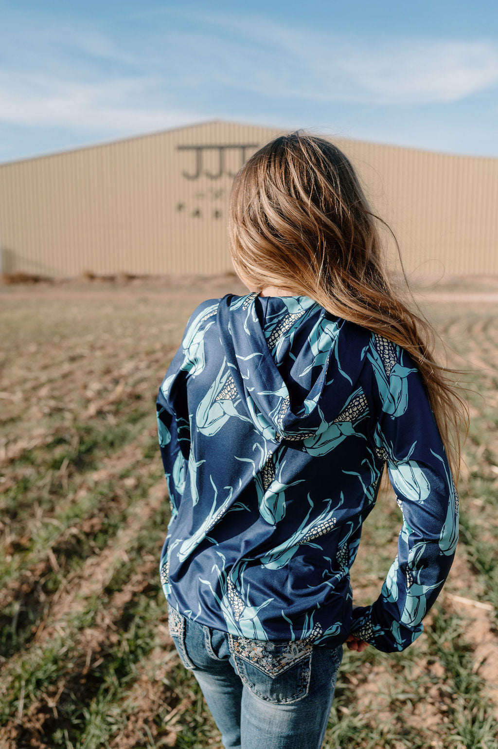 girl wearing navy performance hoodie with large ears of corn all over it