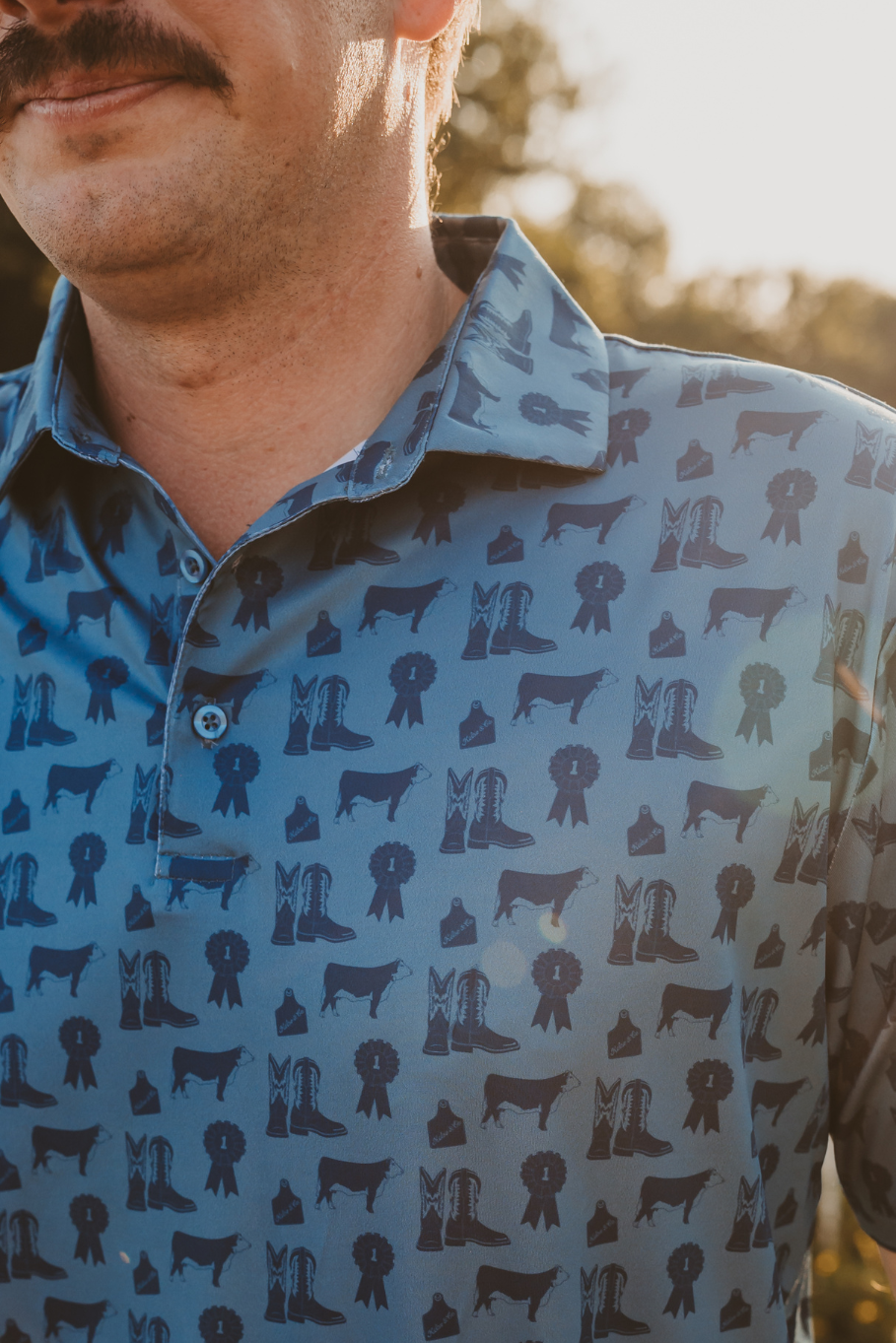 close up county fair mens performance polo in blue with hereford cattle, cowboy boots and blue ribbons