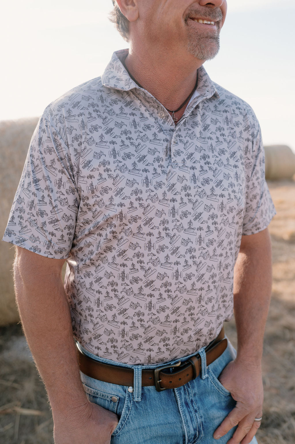 man wearing a light gray performance polo with a dark gray antique tractor print