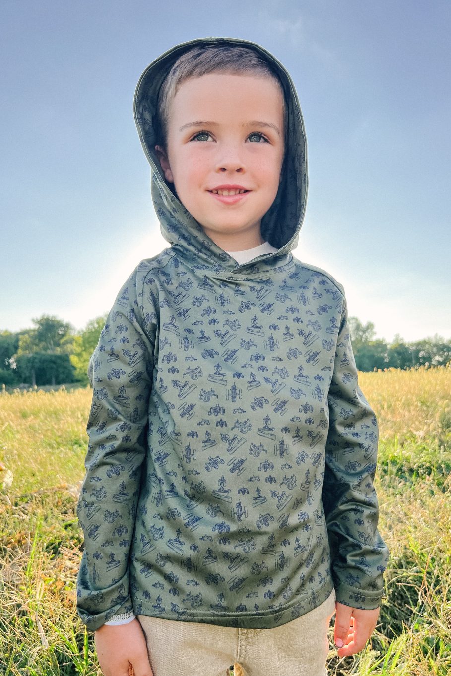 boy wearing performance hoodie with hood up in a field of grass