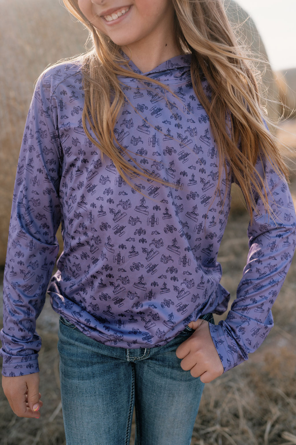 girl on a farm wearing a purple performance hoodie with dark purple antique tractor pattern