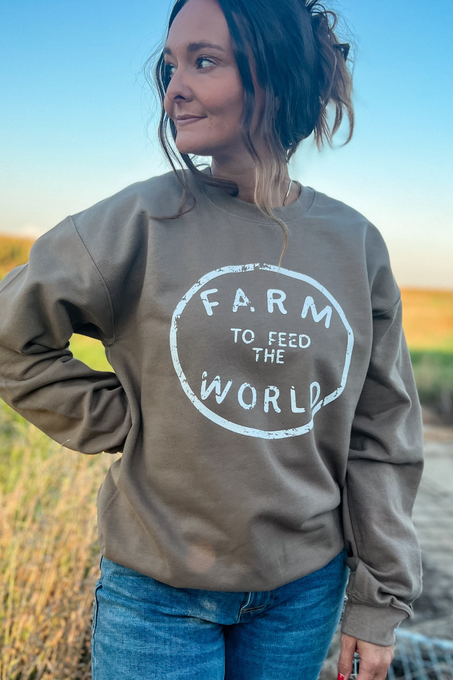 girl on a farm wearing a unisex crewneck in brown that says farm to feed the world