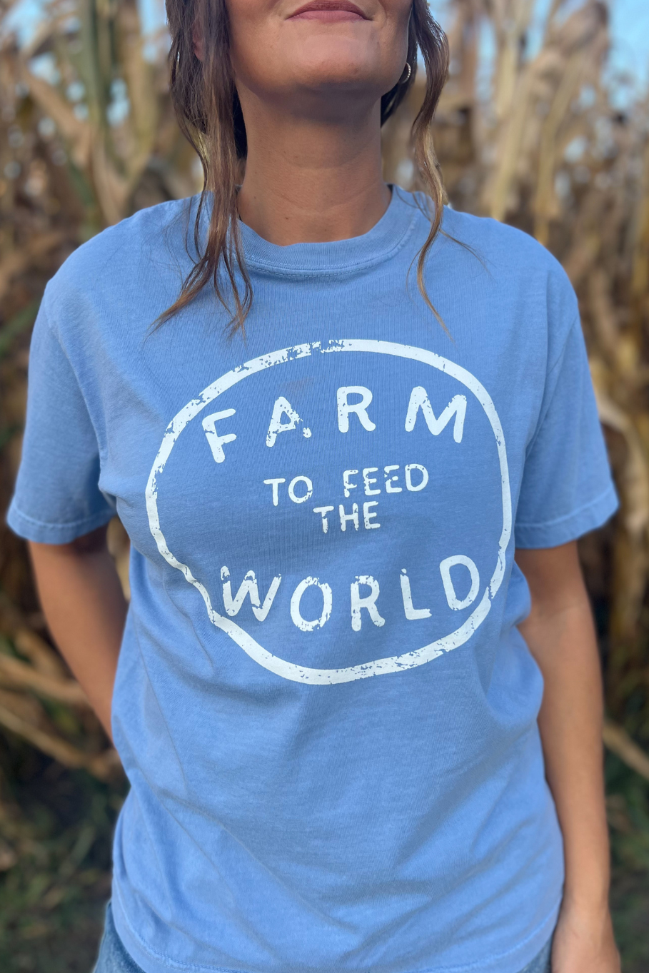 girl standing in front of a corn field with farm to feed the world in blue shirt on