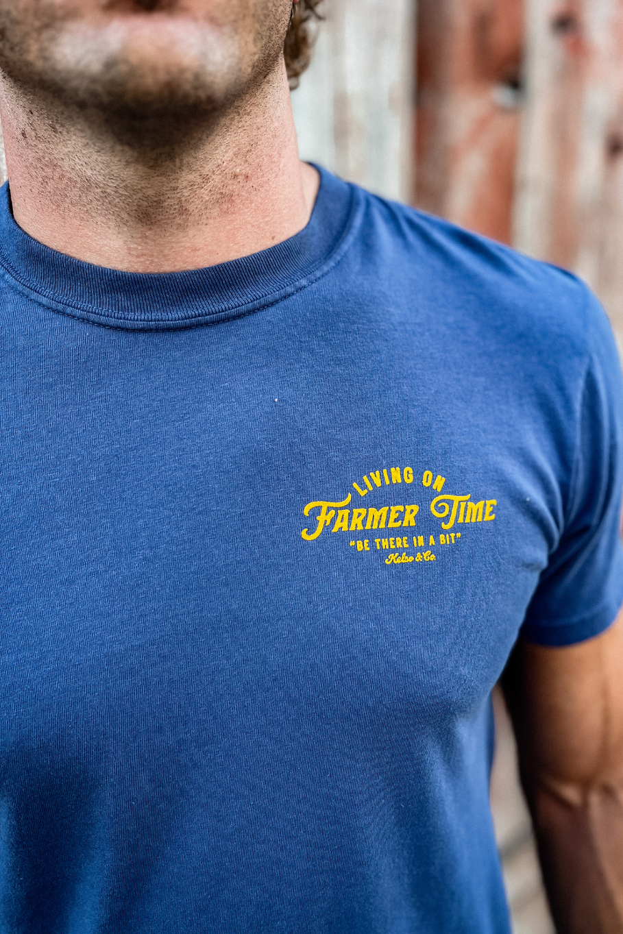 Man wearing a blue t-shirt with yellow text, standing against a wooden fence.