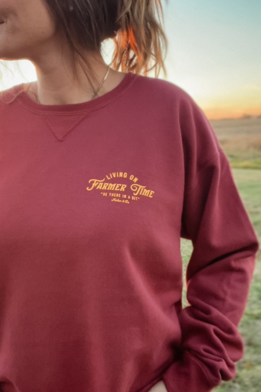 girl wearing crewneck on a farm that says living on farmer time