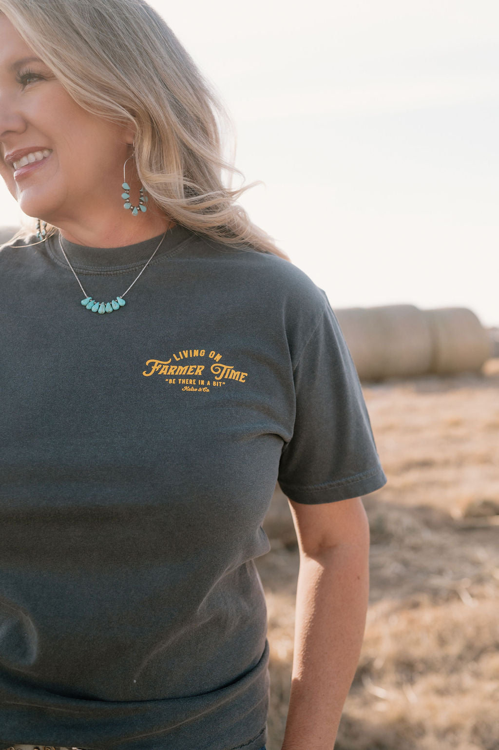 women on a farmer wearing a dark gray tshirt that says "living on farmer time" on the left chest in yellow