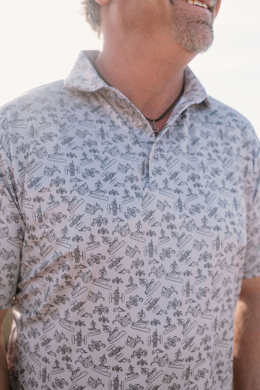 man wearing a light gray performance polo with a dark gray antique tractor print