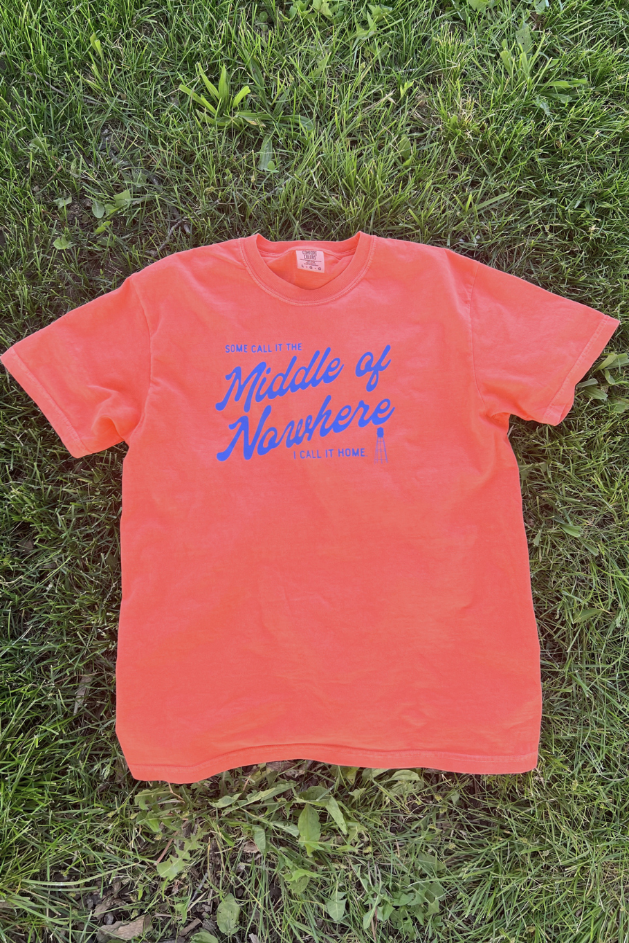 bright salmon comfort colors tshirt with blue  graphic "some call it the middle of nowhere I call it home" with a water tower graphic