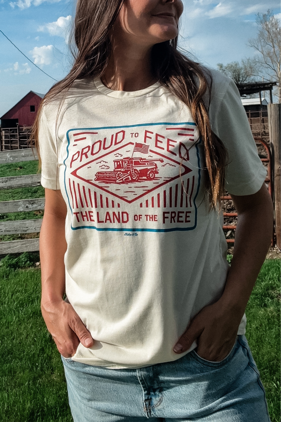 woman wearing a natural colored tshirt with a red and blue patriotic graphic of a combine with an American Flag "Proud to feed the land of the free"
