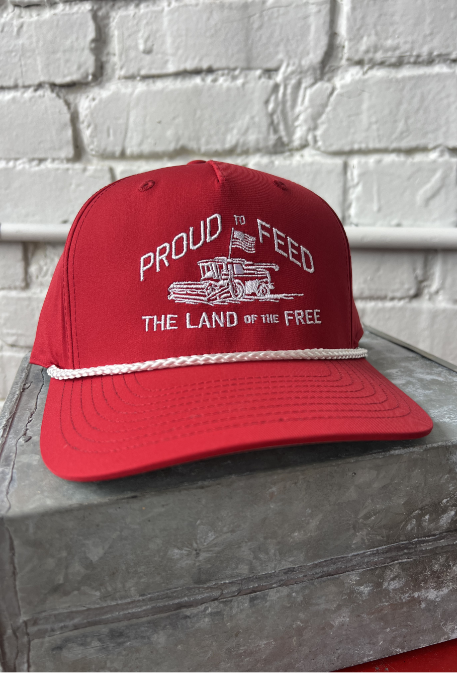 red rope retro trucker hat with white embroidery of a combine flying an American flag