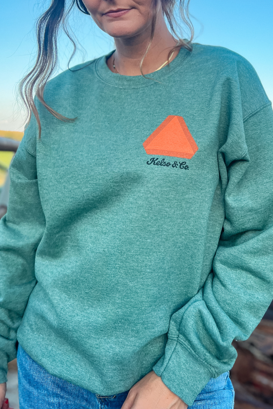 front of save a farmer crewneck in heather green with a left crest print of a slow moving vehicle sign and the kelso and co. logo