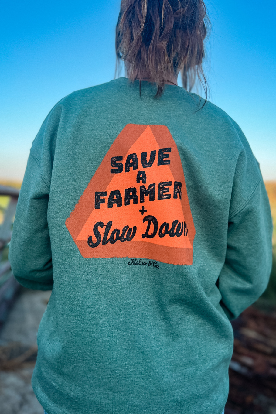 back heather green unisex crewneck with a slow moving vehicle sign and text "save a farmer + slow down"