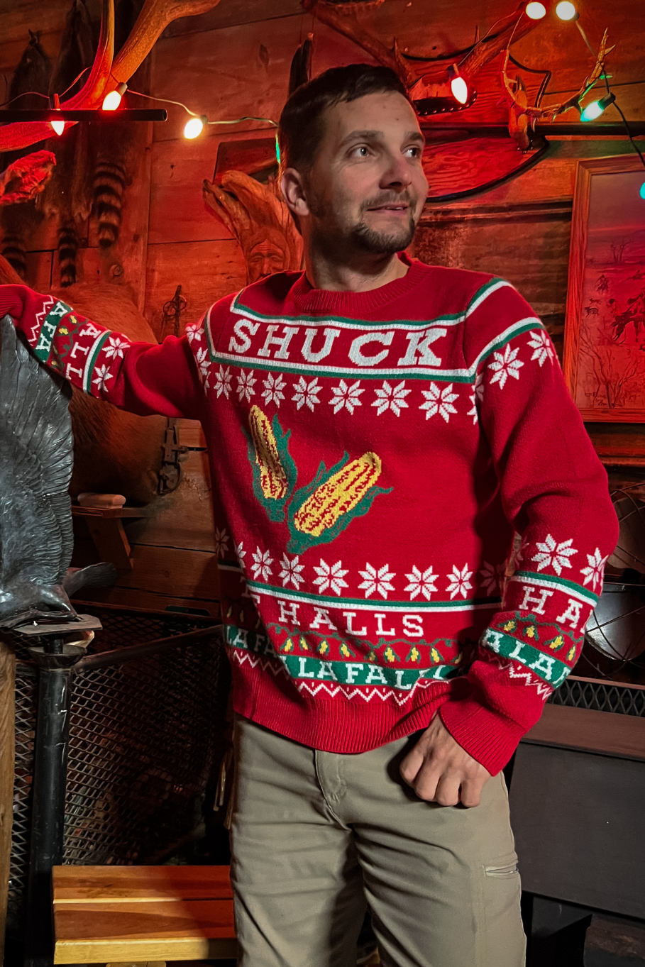 guy wearing red holiday sweater that says shuck the halls with corn inside a cabin