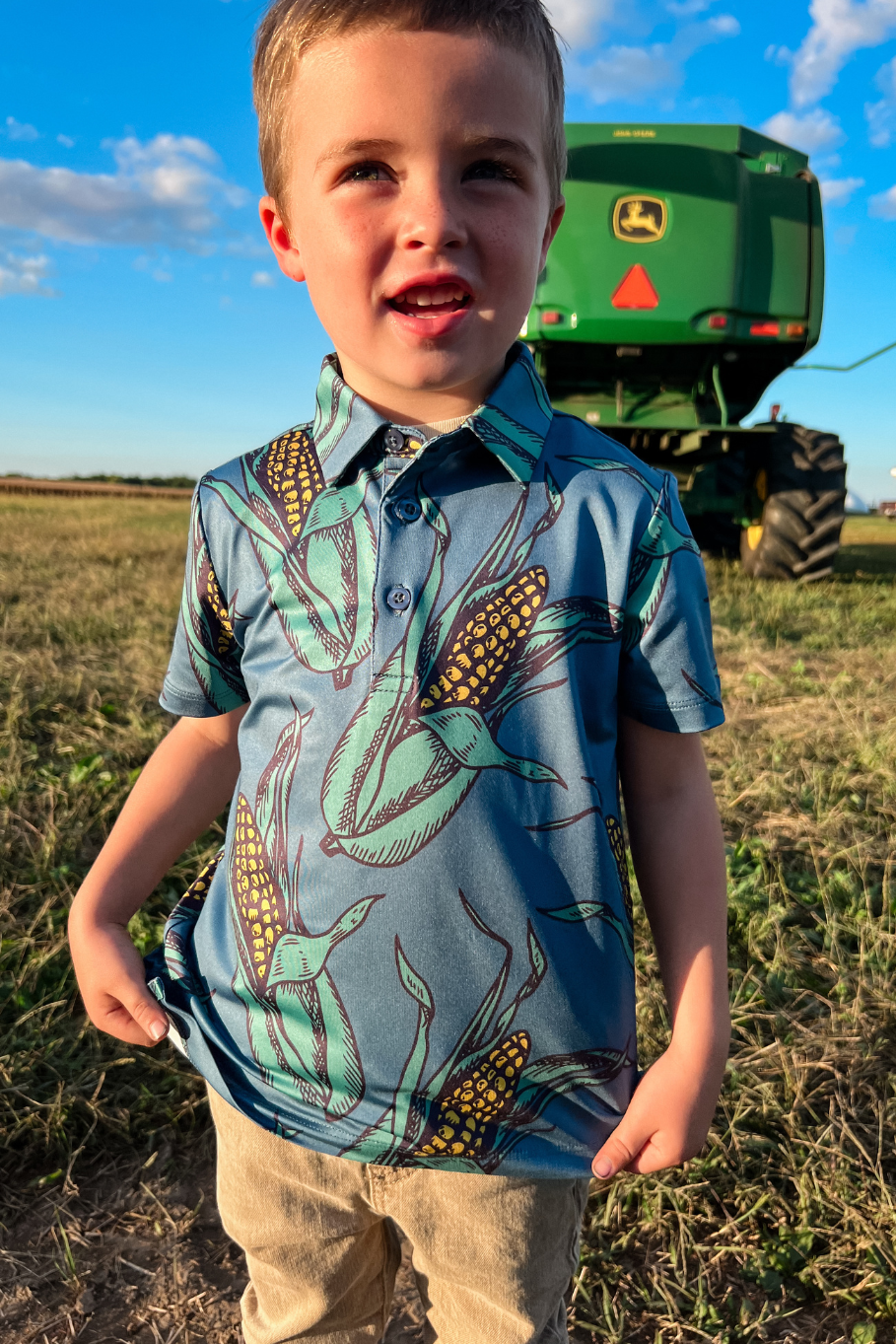 boy in a corn polo standing behind a john deer combine
