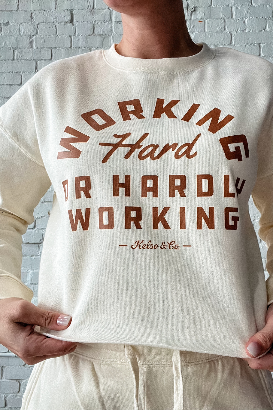 close up of bone cropped crewneck that says working hard or hardly working in brown